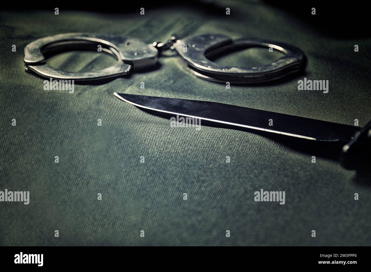Handschellen und Messer auf einem schwarzen Tisch. Gewalt, Mord, militärisches Konzept. Gemischte Medien Stockfoto