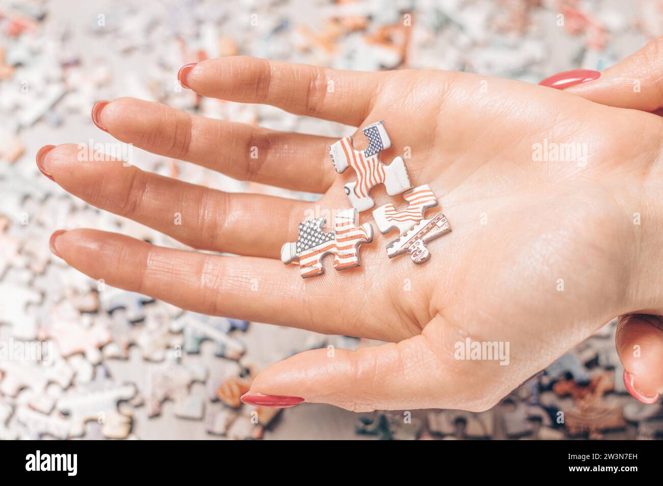Frau, die drei Puzzles mit der US-Flagge auf der Hand hat. Wirtschaftliches und politisches Konzept. Gemischte Medien Stockfoto