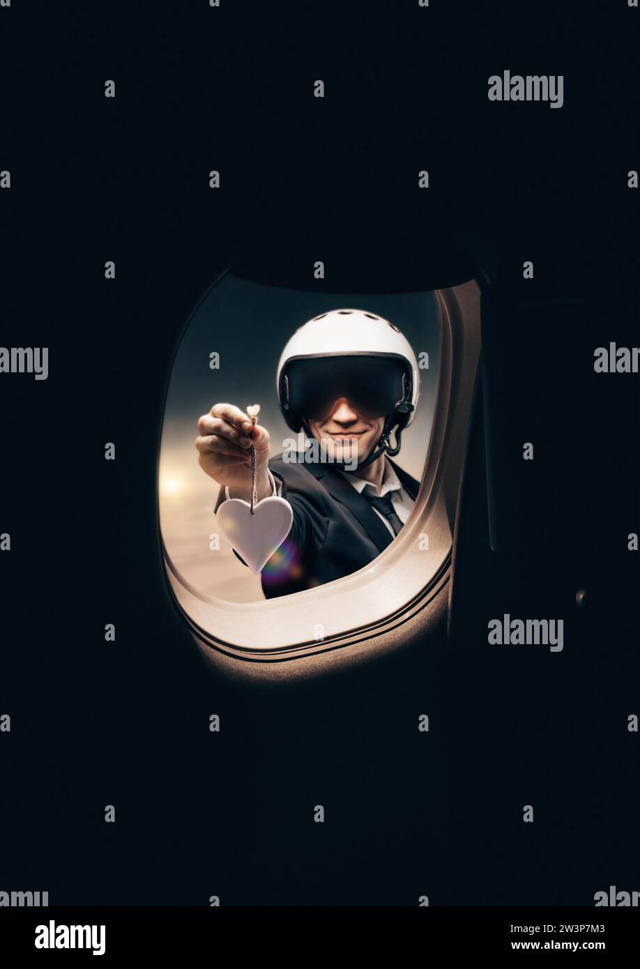 Porträt eines Mannes in einem Helm. Er schaut in das Bullauge eines Flugzeugs und hält eine Herzfigur aus. Reise- und Versicherungskonzept. Gemischt Stockfoto
