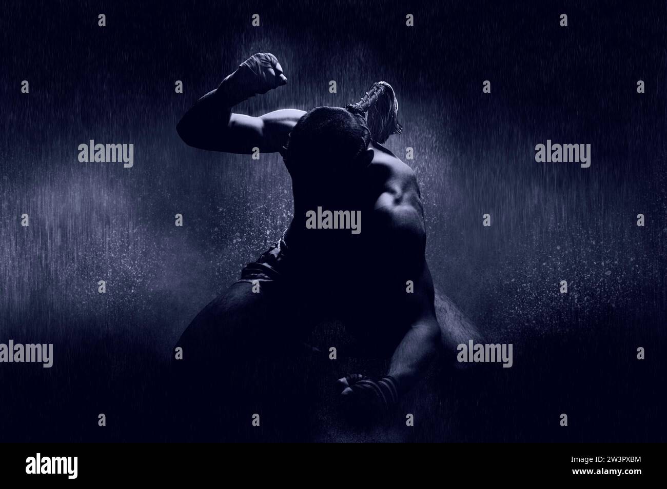 Thai Boxer im Regen und unter blauem Spotlight. Mongkhon. Das Konzept des Sieges bei Wettkämpfen, illegale Turniere. Gemischte Medien Stockfoto