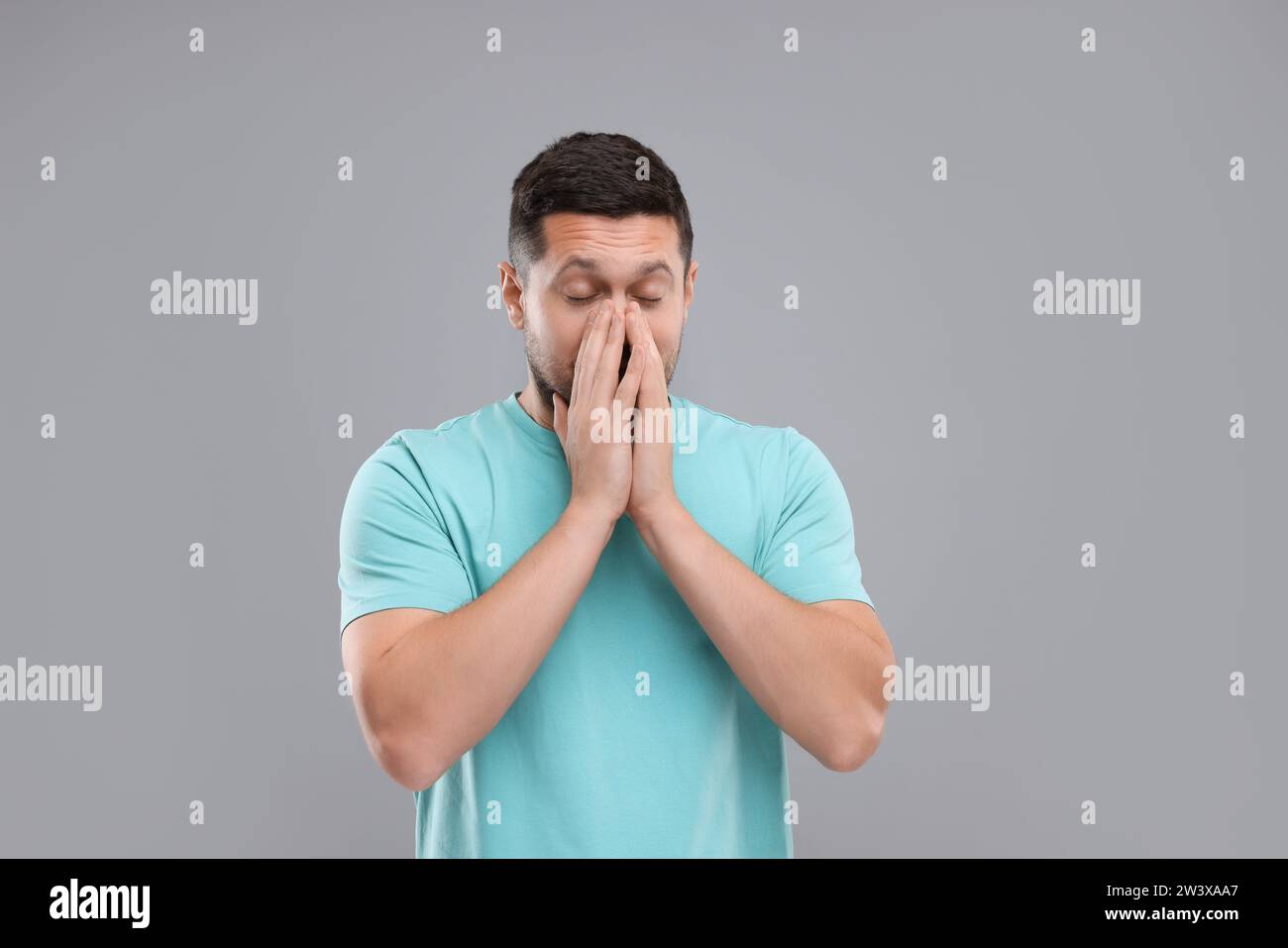 Allergiesymptom. Mann niest auf hellgrauem Hintergrund Stockfoto