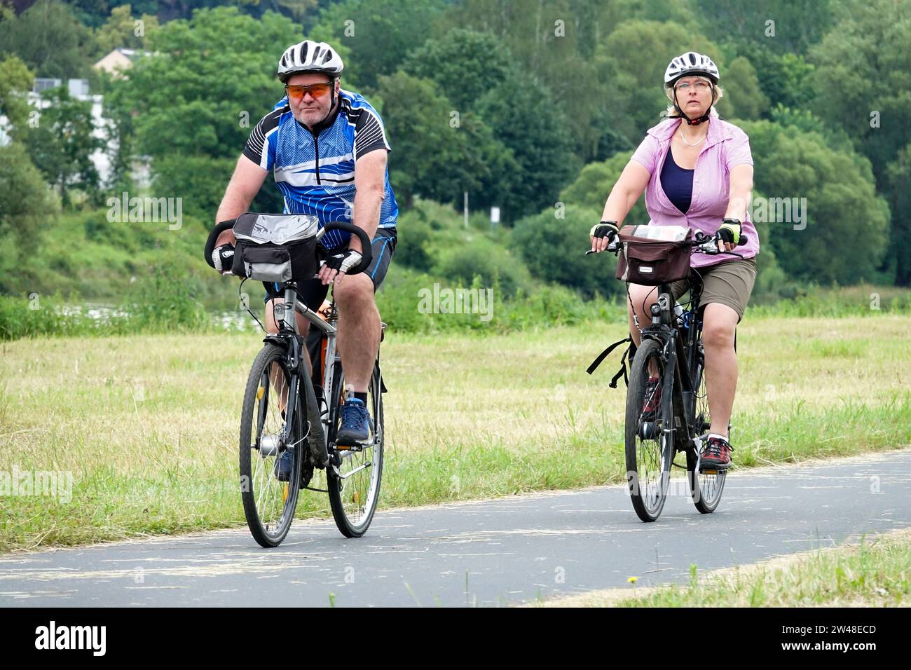 Ein Paar, ein Mann und eine Frau, fahren mit dem Fahrrad auf einem Radweg in einer Landschaft mit gemähter Wiese Stockfoto