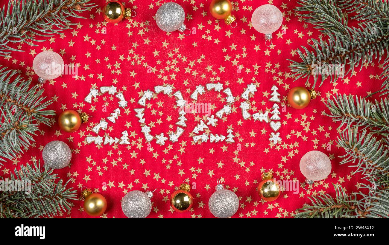 Neujahrsdatum 2024 arrangiert aus Weihnachtskuchenkeksen auf rotem Tischtuch, verziert mit Ornamenten und Kranz Stockfoto