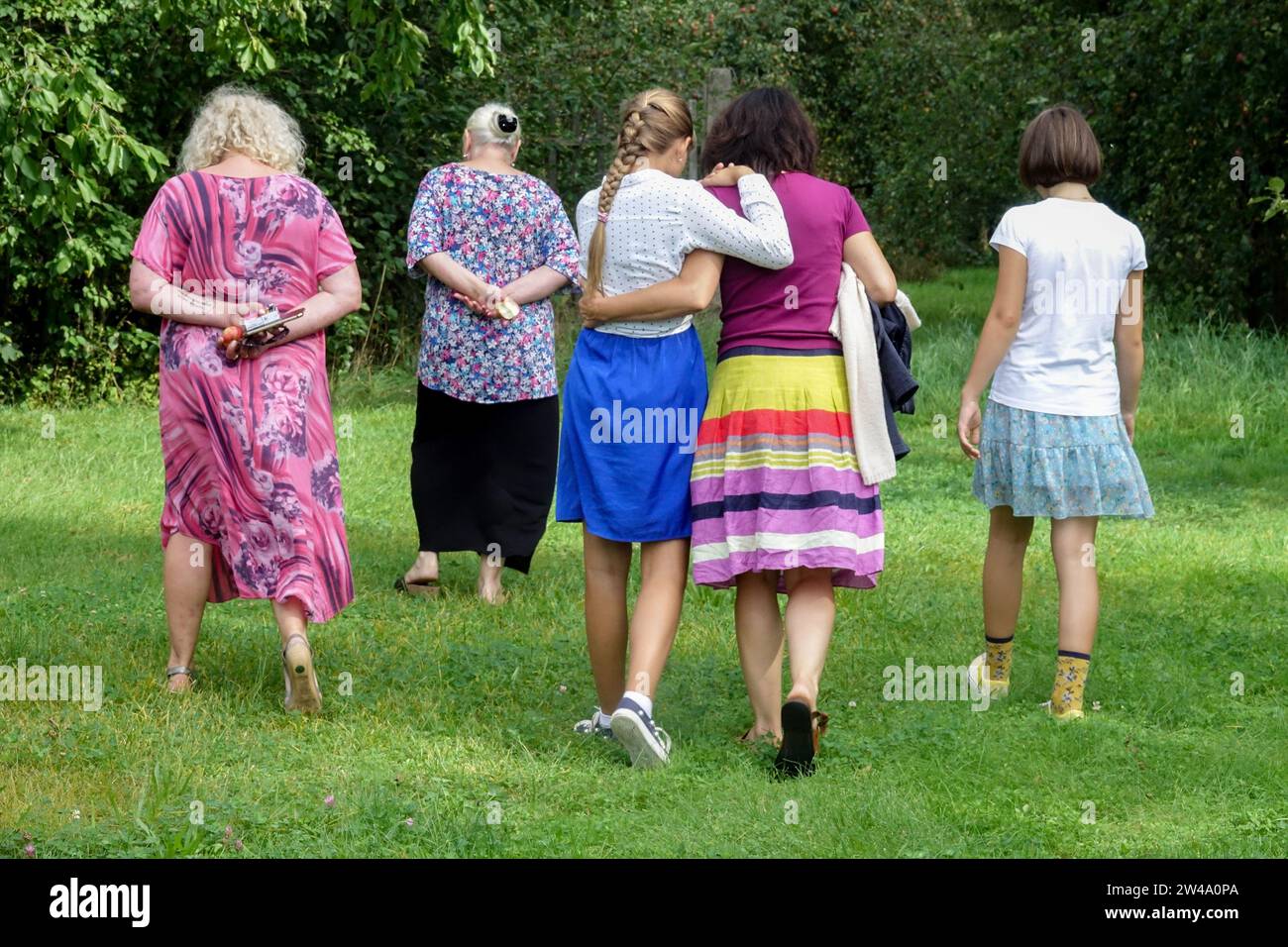 Fünf Frauen verschiedener Generationen gehen auf dem Gartenrasen nach hinten Stockfoto