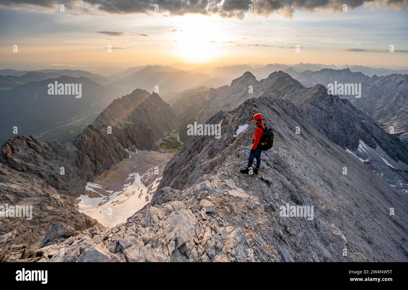 Bergsteiger mit Helm auf einem schmalen Bergrücken bei Sonnenaufgang, Überquerung des Jubilaeumsgrat, Blick auf das Hoellental mit Hoellentalferner und Alpspitze Stockfoto