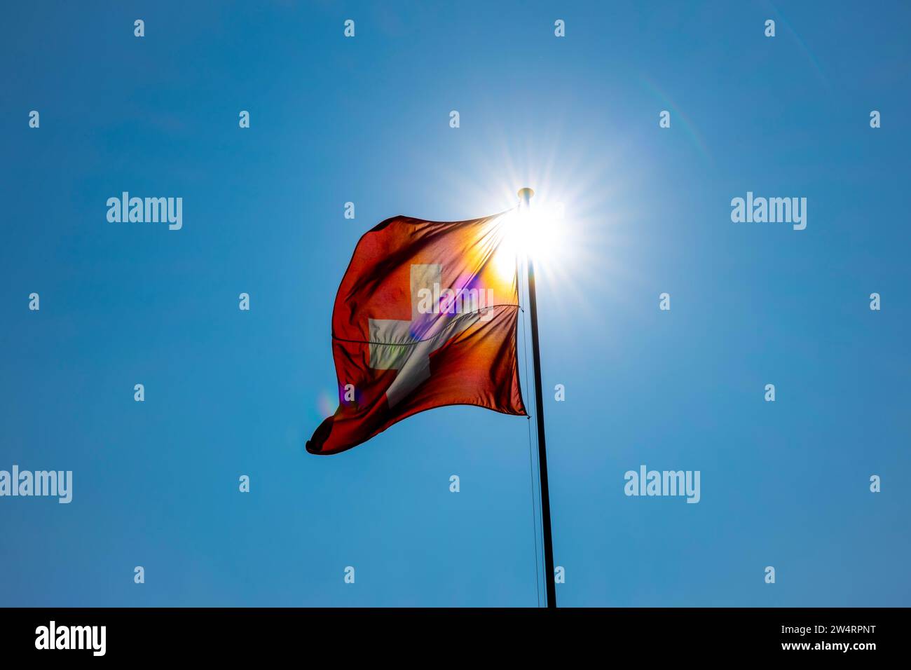 Wunderschöne Schweizer Flagge gegen Blue Clear Sky und Sunbeam an einem windigen Tag in der Schweiz Stockfoto