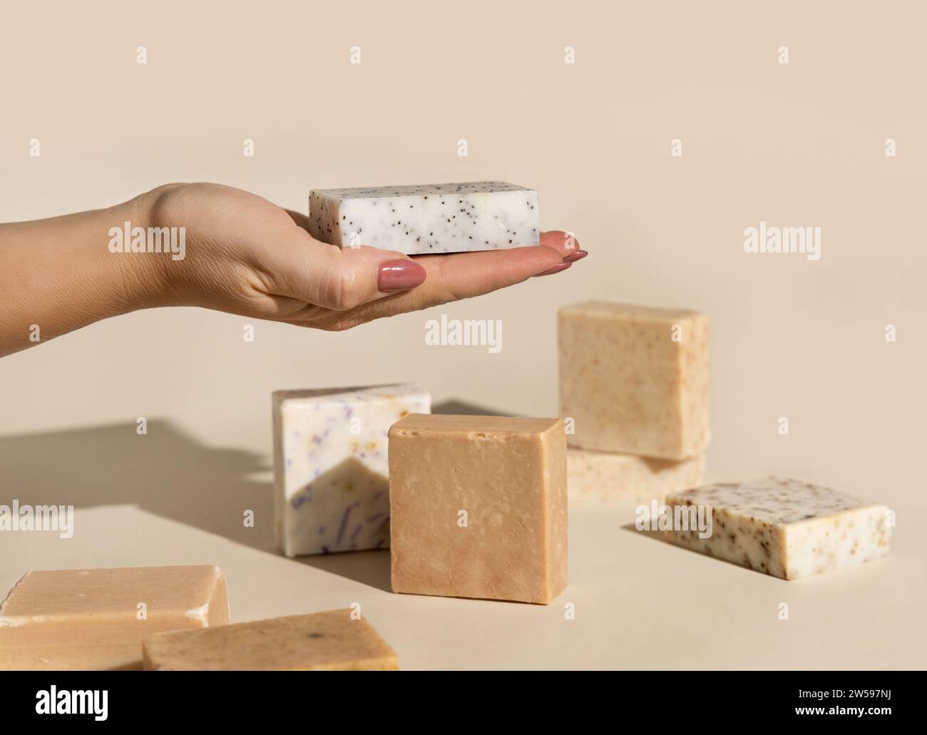 Hand hält naturbeige Seifenstäbe mit leerem Etikett auf hellbeigen, Nahaufnahme, harten Schatten. Hygieneprodukte für Spa und Hautpflege. Mit organischer Hand Stockfoto