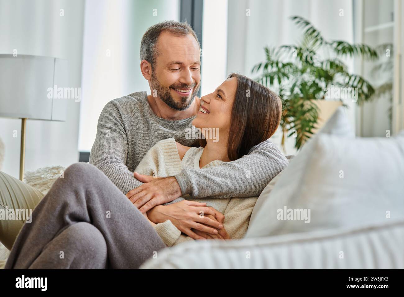 Fröhliches, kinderfreies Paar, das sich auf der Couch im Wohnzimmer ansieht, Liebe und Freude Stockfoto