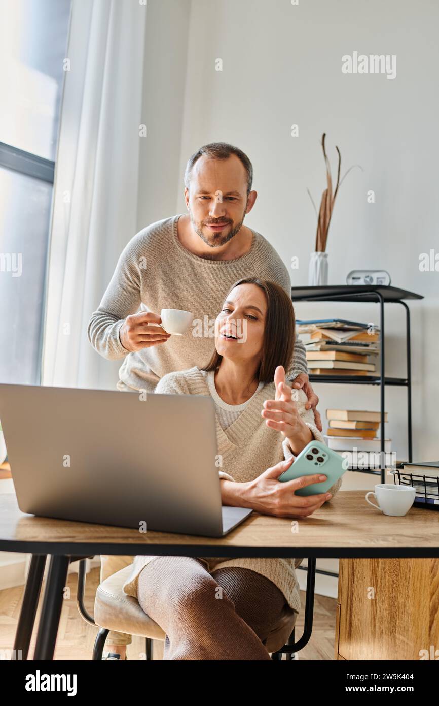 Fürsorglicher Ehemann mit Kaffeetasse, Unterstützung der Frau, die zu Hause am Laptop arbeitet, Einheit eines kinderfreien Paares Stockfoto