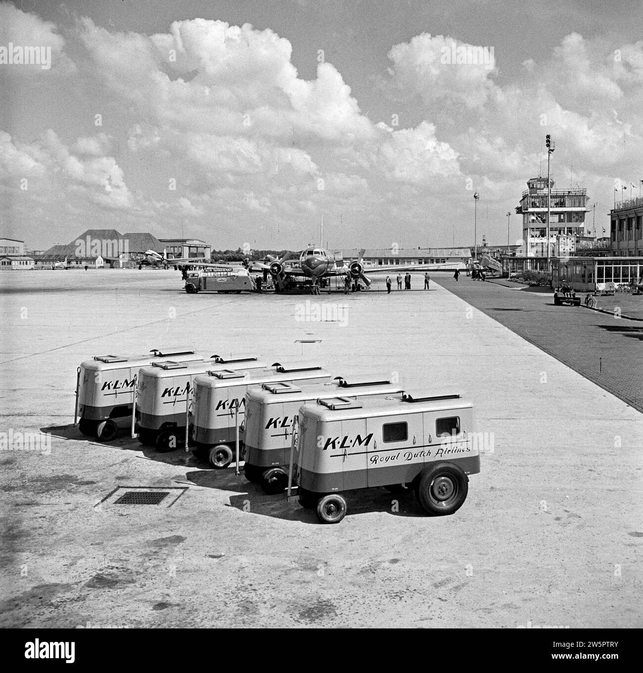 Geparkte Passagierflugzeuge am Flughafen Schiphol, fünf KLM-Batterieautos im Vordergrund. Der Kontrollturm rechts ca. August 1951 Stockfoto