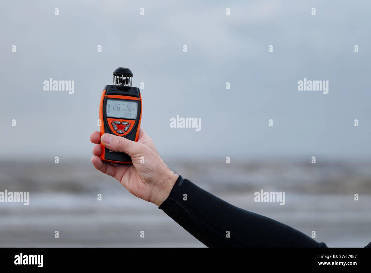 UK. Ein Mann, der am Strand steht und ein digitales Anemometer hält, um die aktuelle Windgeschwindigkeit, -Richtung und -Temperatur zu messen Stockfoto