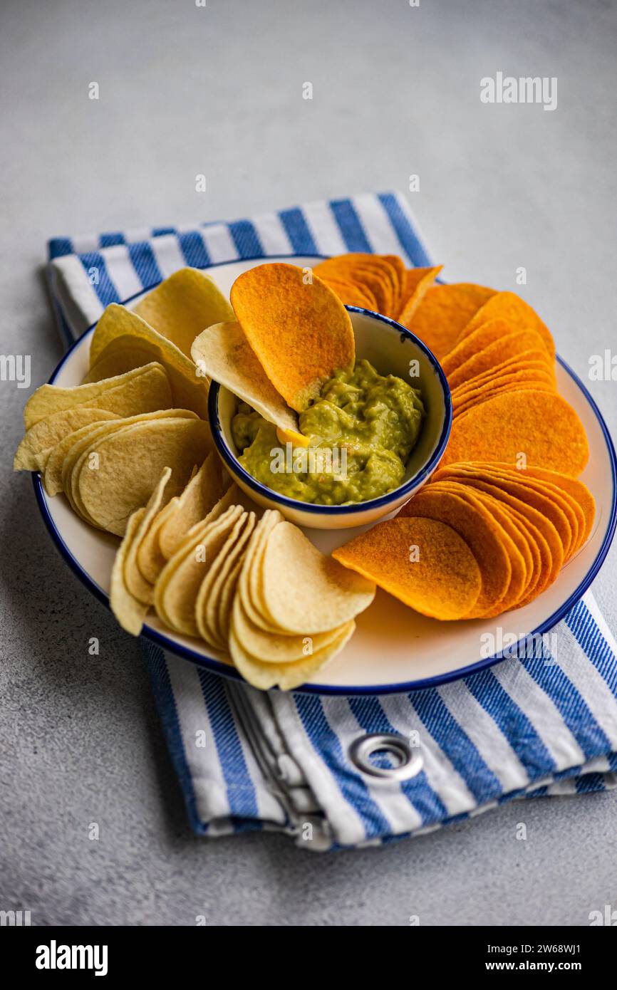 Blick von oben auf den Teller mit verschiedenen Chips, einschließlich Kartoffeln, Paprika und Käse, serviert mit einer Schüssel mit frischer Avocado-Guacamole auf einer gestreiften Serviette Stockfoto