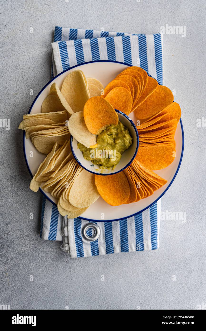 Blick von oben auf den Teller mit verschiedenen Chips, einschließlich Kartoffeln, Paprika und Käse, serviert mit einer Schüssel mit frischer Avocado-Guacamole auf einer gestreiften Serviette Stockfoto