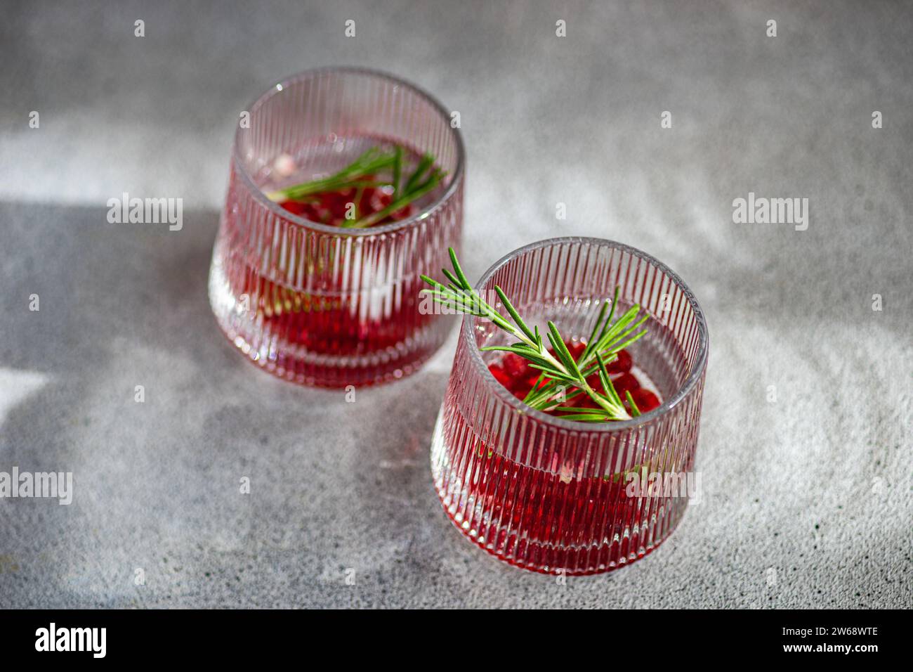 Von oben aus Kristallgläsern mit Gin Tonic und Granatapfel, garniert mit Rosmarin, werfen weiche Schatten auf eine graue Betonoberfläche Stockfoto