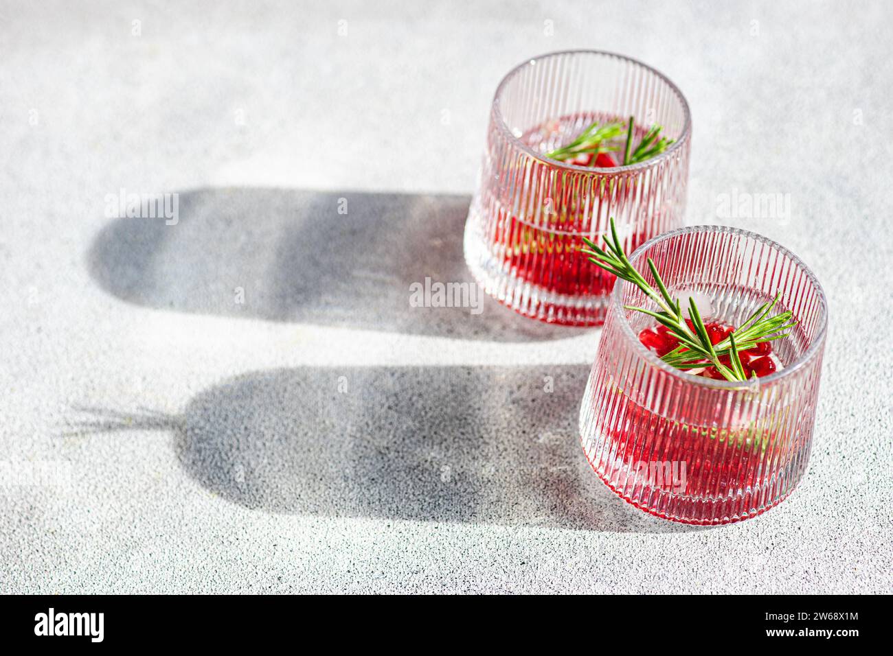 Von oben genießen Sie sonnendurchflutete Gin Tonic-Cocktails mit Granatapfel und Rosmarin in strukturierten Gläsern auf einer hellen Oberfläche Stockfoto