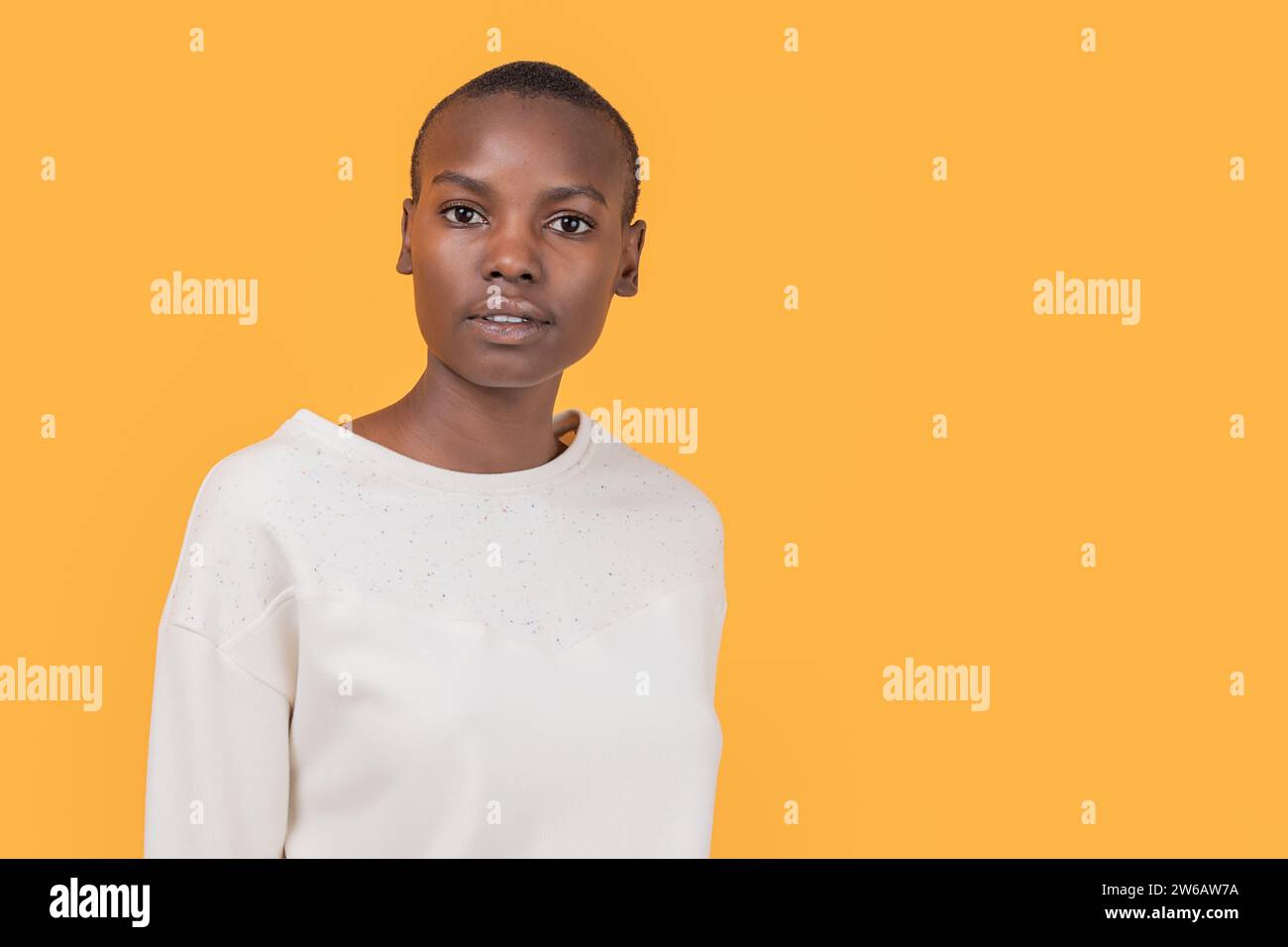 Selbstbewusste, schlanke afroamerikanische junge Frau in modischer Freizeitkleidung, die auf die Kamera blickt, während sie vor gelbem Hintergrund steht Stockfoto