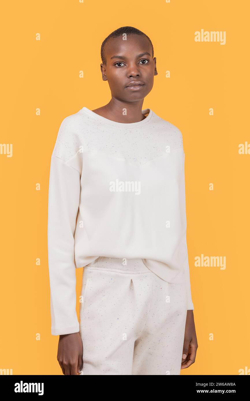 Selbstbewusste, schlanke afroamerikanische junge Frau in modischer Freizeitkleidung, die auf die Kamera blickt, während sie vor gelbem Hintergrund steht Stockfoto
