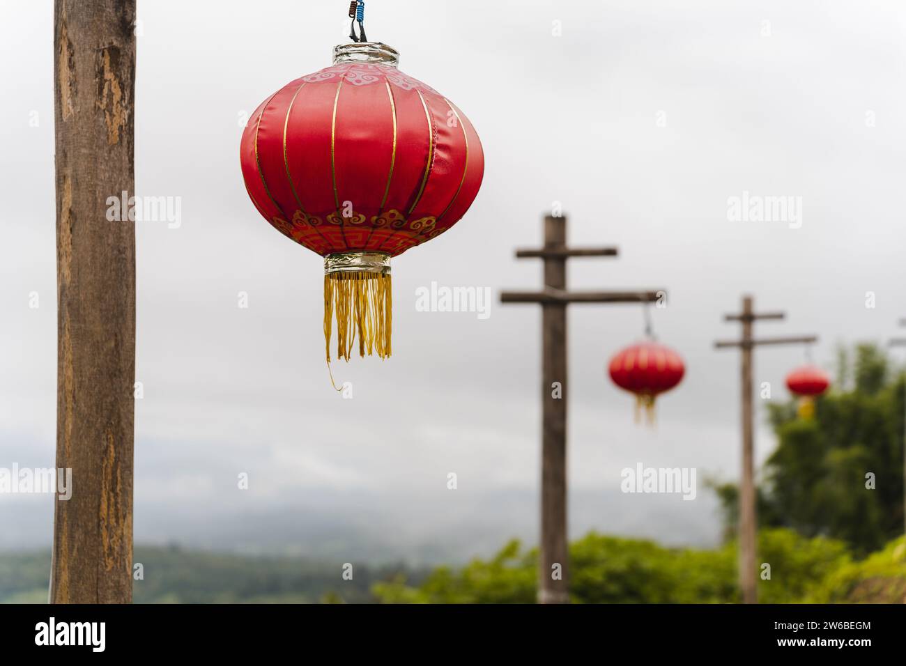 Traditionelle rote chinesische Laternen hängen während der Feiertage an Holzpfählen vor bewölktem Himmel in Thailand Stockfoto