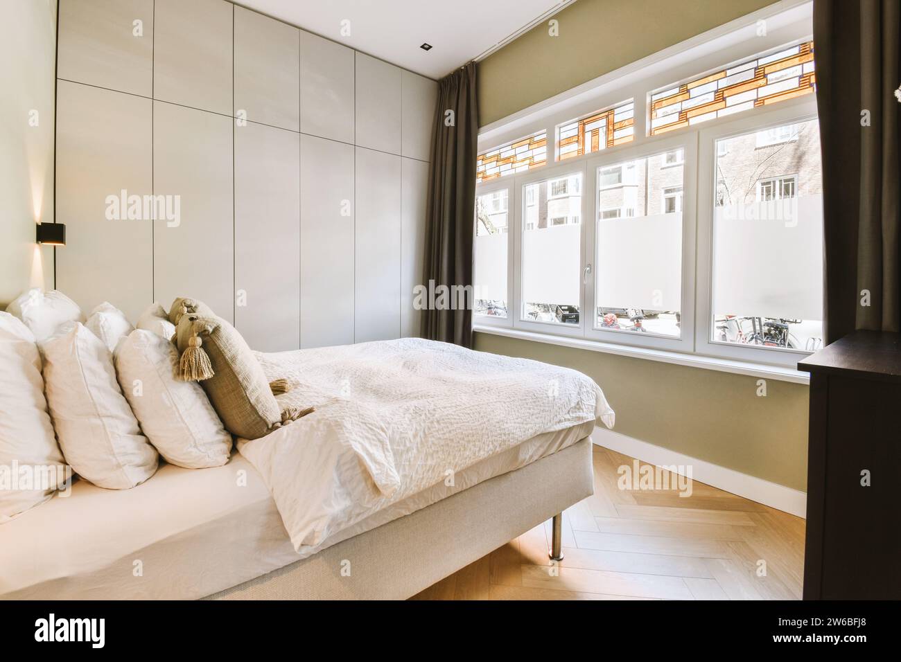 Innenraum des komfortablen Schlafzimmers mit weißem Bett vor einem großen hellen Fenster in einem modernen Apartment Stockfoto