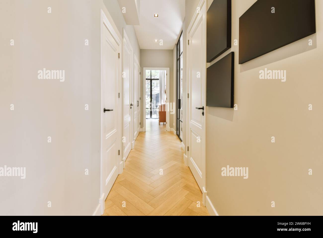 Innenraum des leeren langen Flurs mit weißer Wand und geschlossenen Türen von Zimmern mit Parkettboden im modernen Haus Stockfoto