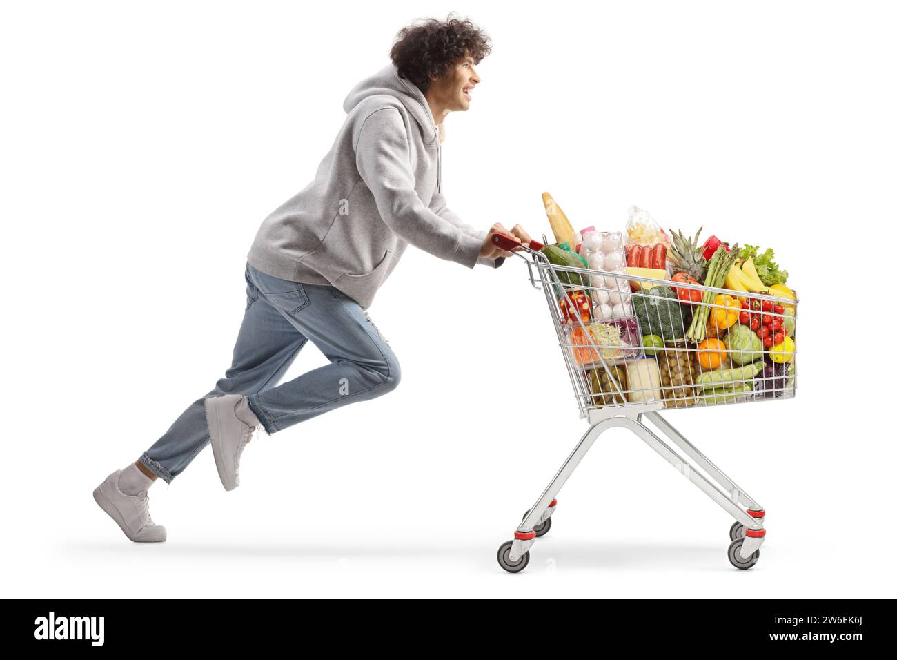 Junger Mann, der mit Essen in einem Einkaufswagen läuft, isoliert auf weißem Hintergrund Stockfoto