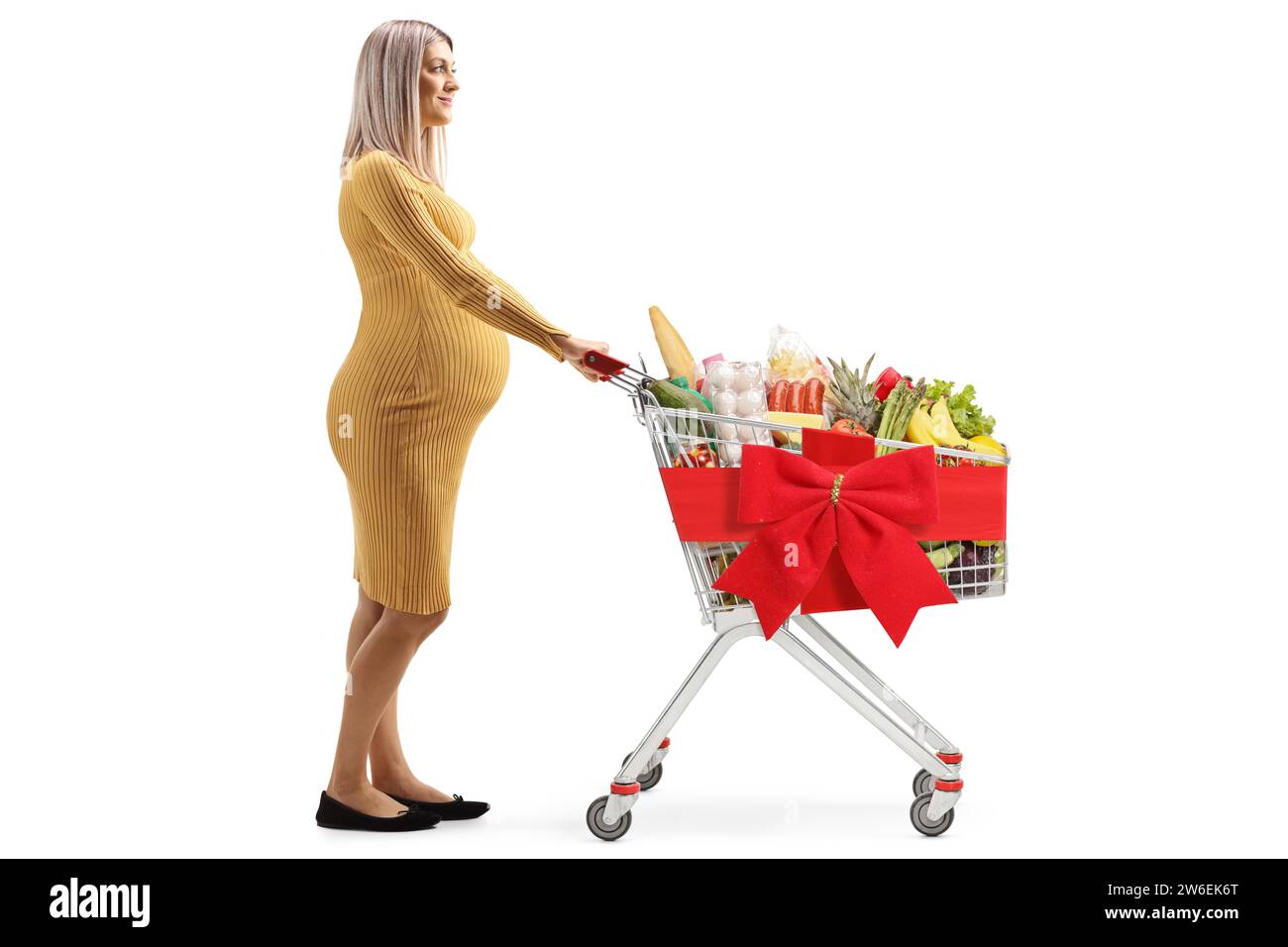 Profilaufnahme einer schwangeren Frau, die einen Einkaufswagen mit roter Schleife auf weißem Hintergrund schiebt Stockfoto