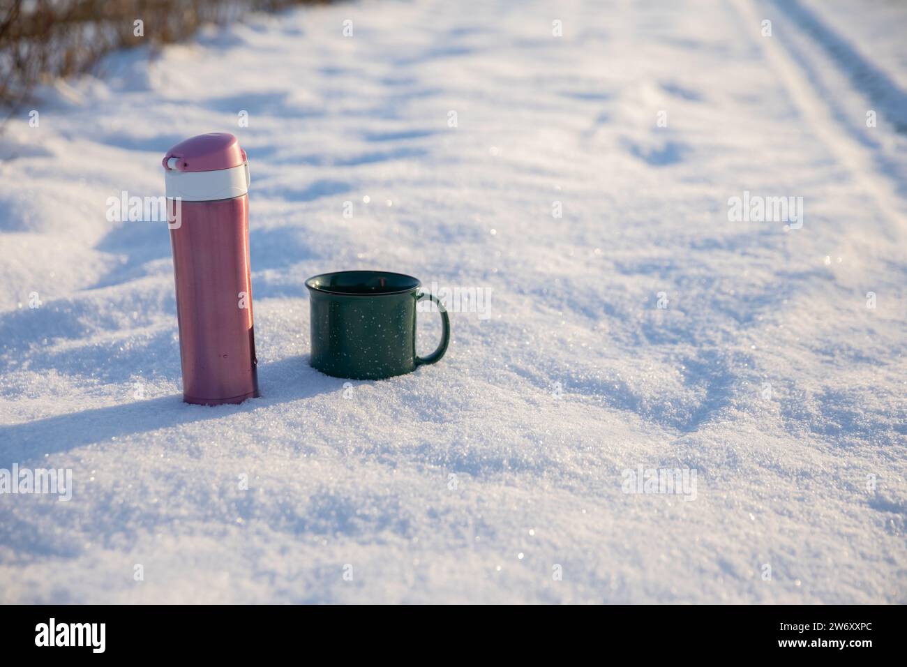 Eine Thermoskanne und eine Tasse stehen auf einer schneebedeckten Feldstraße. Stockfoto
