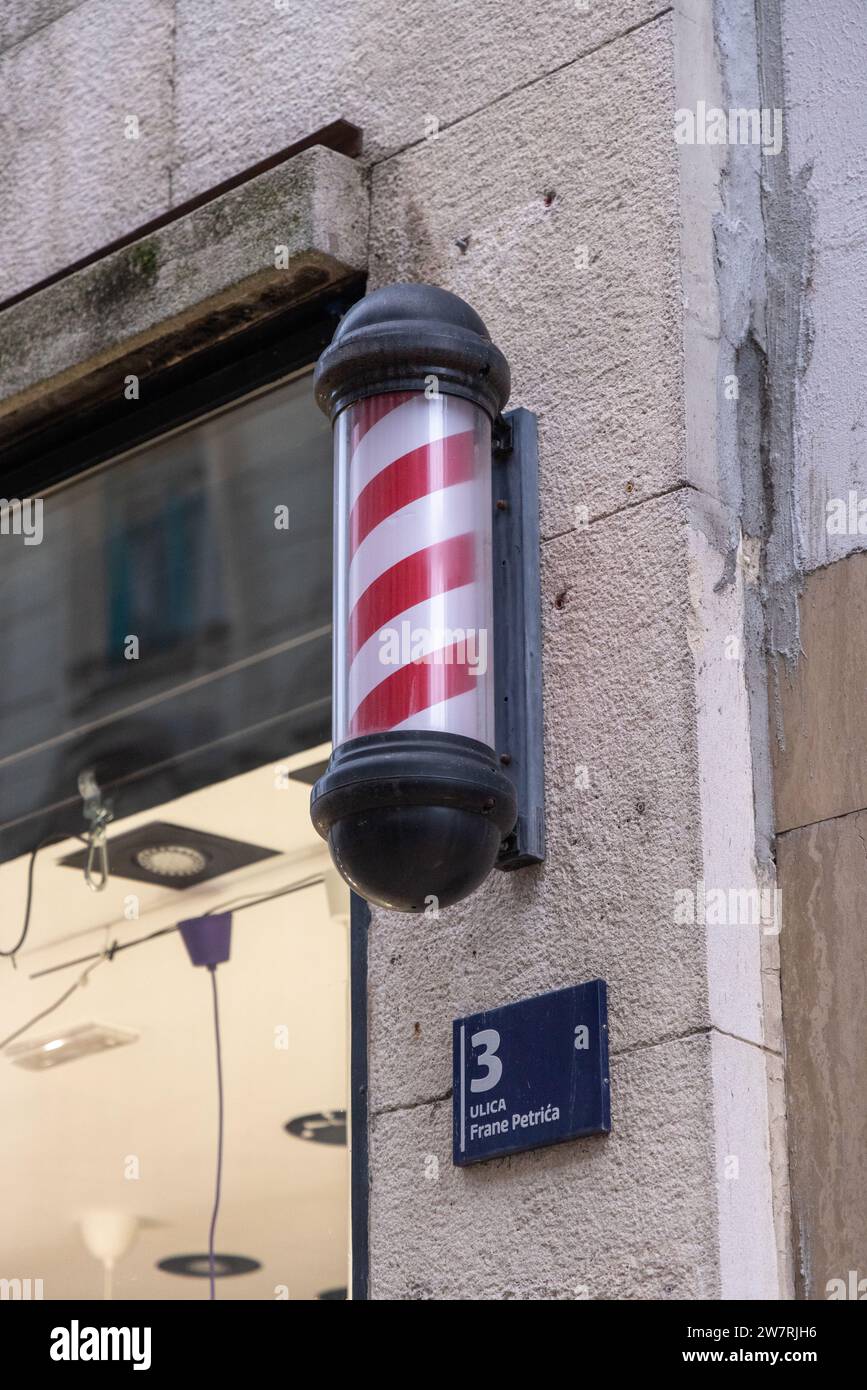 Friseurstange, traditionelles Zeichen für einen Friseurladen: Rotierender Zylinder mit roten Diagonalstreifen (schraubenförmige Streifen); Friseurschild an der Fassade des Friseurshops Stockfoto