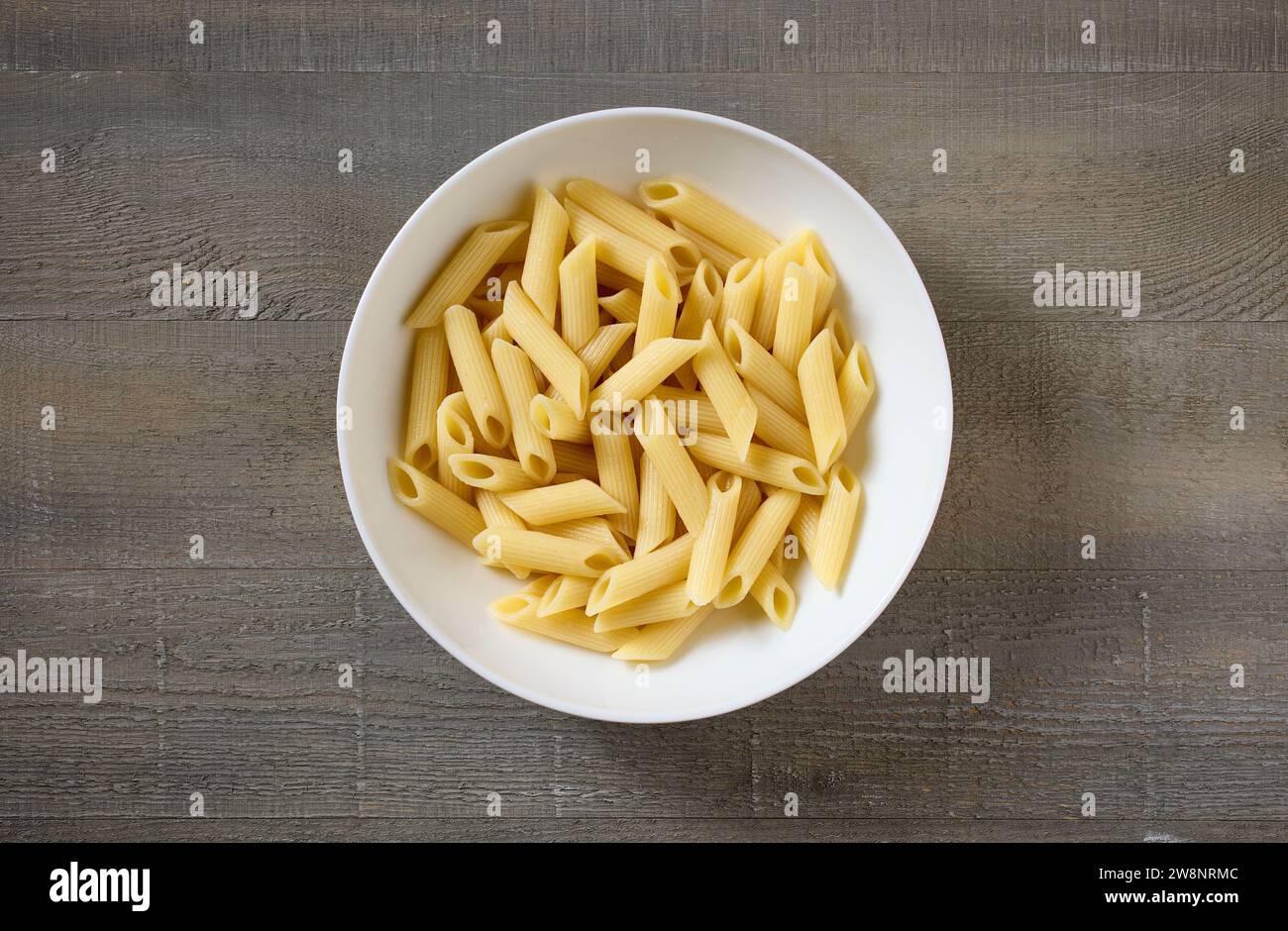 Schüssel mit gekochter Pasta Penne auf hölzernem Küchentisch, Blick von oben Stockfoto