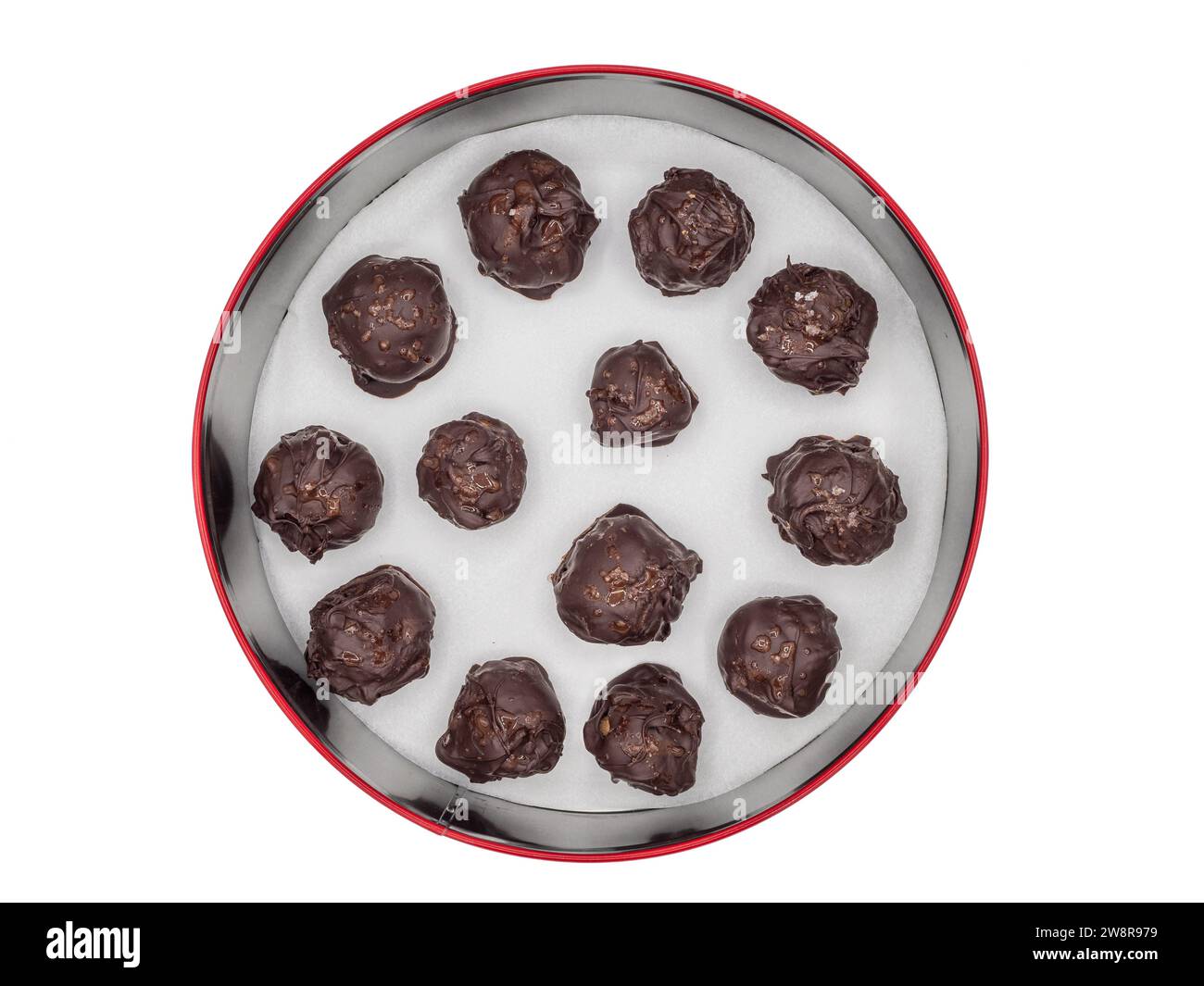 Runder Behälter mit hausgemachten schwedischen Lebkuchenbonbons, mit dunkler Schokolade überzogen und mit Salzflocken bestreut, vor einem weißen Hintergrund. Stockfoto