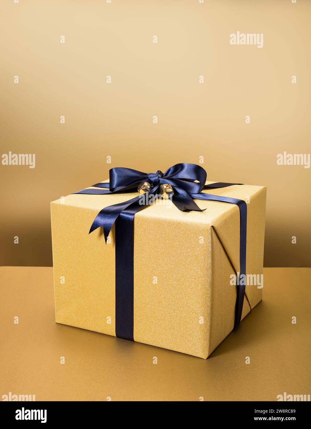 Geschenkverpackung mit goldenem Geschenkpapier und schwarzem Band auf goldenem Hintergrund Stockfoto