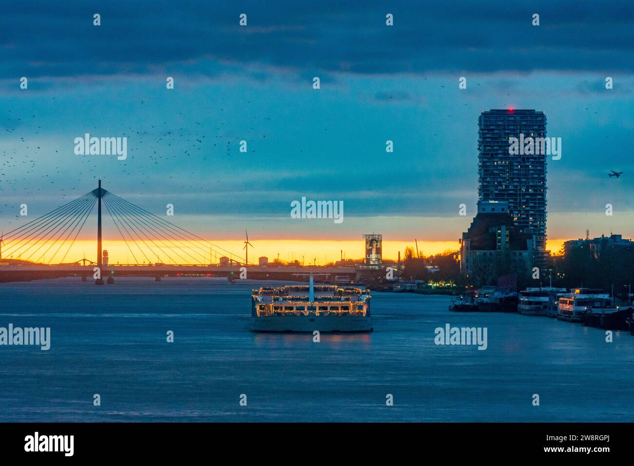 Wien: Sonnenaufgang an der Donau (Donau), Kreuzfahrtschiff in Weihnachtsdekoration, Seilbrücke Donaustadtbrücke, Marina Tower, Flugzeug, BI Stockfoto