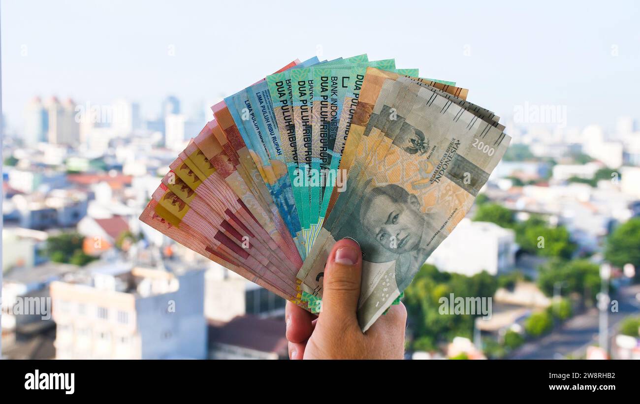 Die Hand des Mannes hält Rupiah-Geld vor dem Hintergrund der Stadt Jakarta. Stockfoto