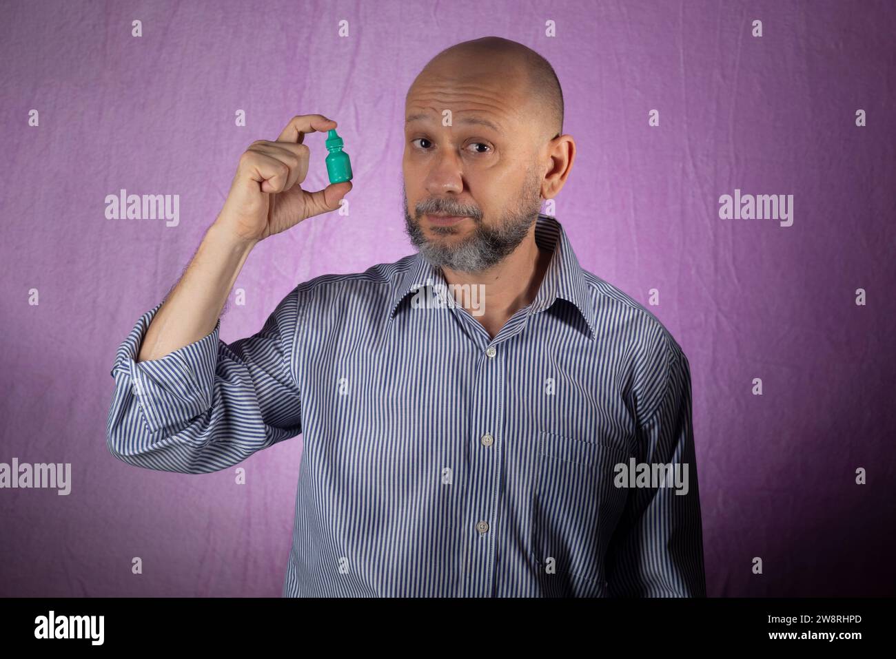 Mann, der grüne Arzneimittelverpackung vor rosa Hintergrund hält. Stockfoto