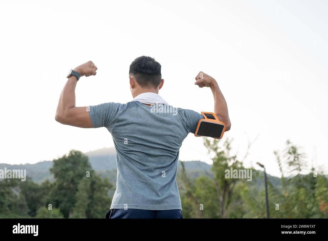 Ein starker asiatischer Mann in Sportbekleidung zeigt seinen starken Armmuskel und läuft im Freien. Rückansicht Stockfoto