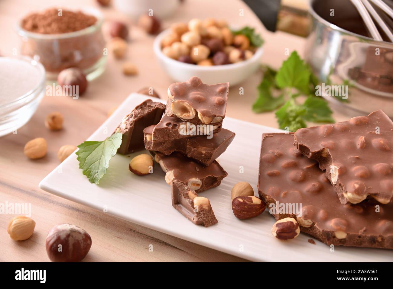 Frisch zubereitete Schokolade mit Haselnüssen auf einem weißen Teller mit Zutaten und Küchenutensilien auf einem Holztisch. Erhöhte Aussicht. Stockfoto