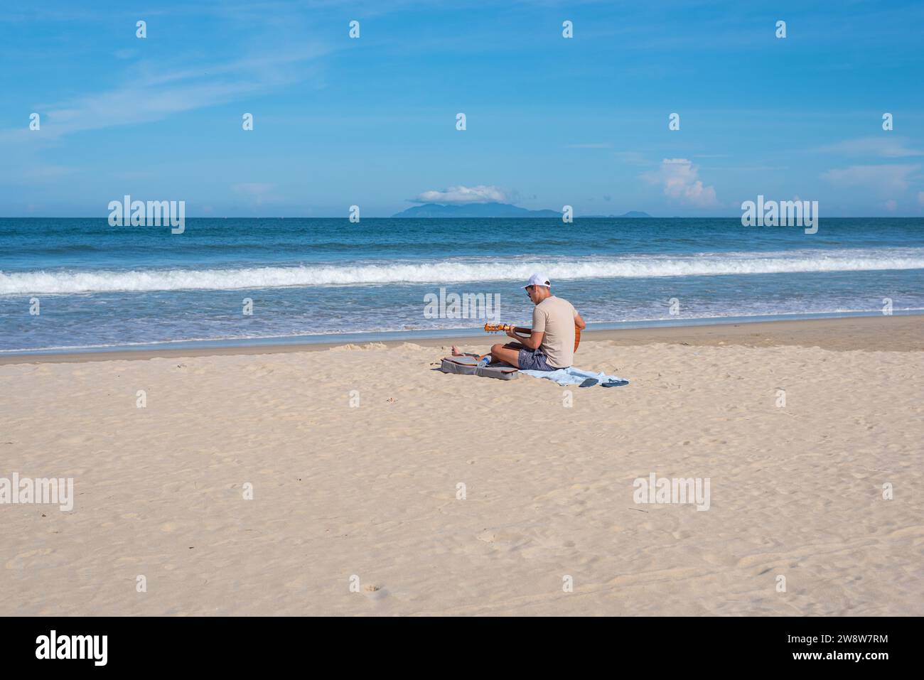 Da Nang, Vietnam - 4. Oktober 2023: Ein männlicher Reisender spielt Gitarre am Strand. Stockfoto