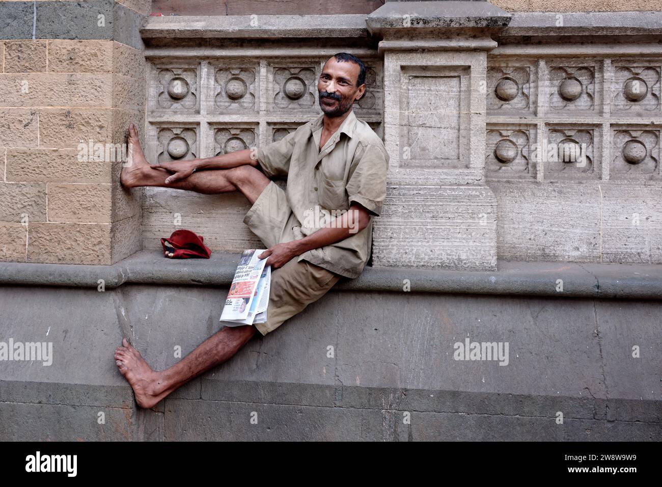 Ein städtischer Straßenreiniger in Mumbai, Indien, hat sich in der Außenwand des Chhatrapati Shivaji Terminus gefunden, um seine Zeitung zu lesen Stockfoto