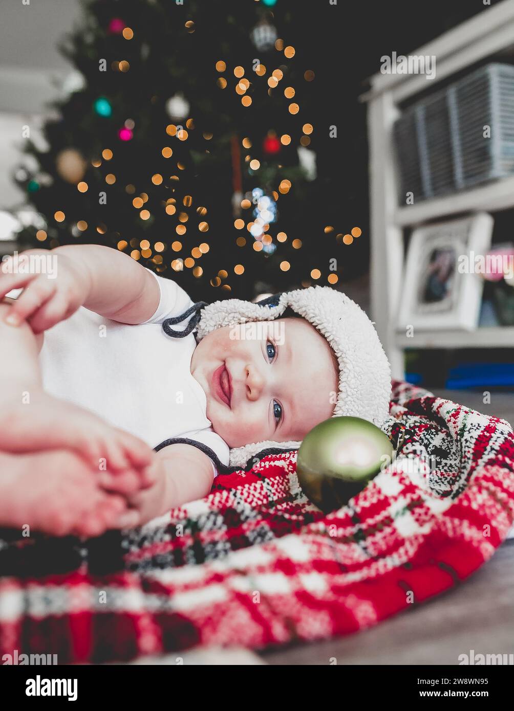 Lächelndes Baby auf Decke mit weihnachtsbaum im Hintergrund Stockfoto