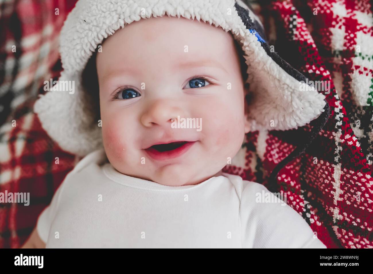 Lächelndes Baby mit weißem Bomberhut auf der Weihnachtsdecke Stockfoto