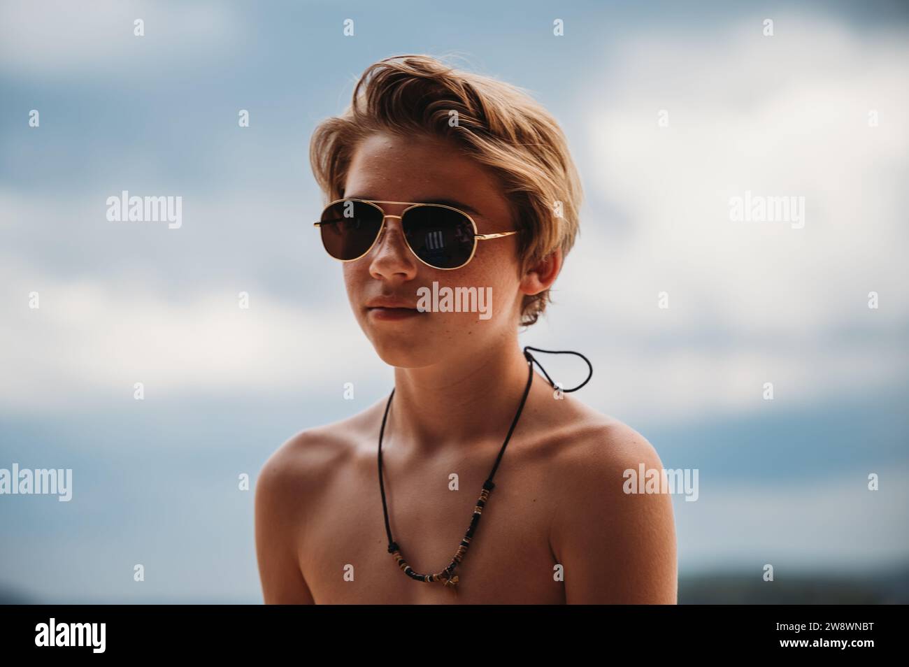 Nahaufnahme eines blonden Teenager-Jungen mit Sonnenbrille und Halskette Stockfoto