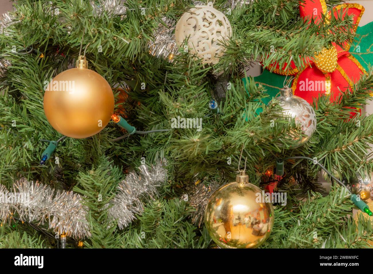 Primer plano de decoracion navidena, bolas doradas y plateadas entre el follaje verde del árbol, pequenas luces, flor de pascua en un fondo borso, c Stockfoto