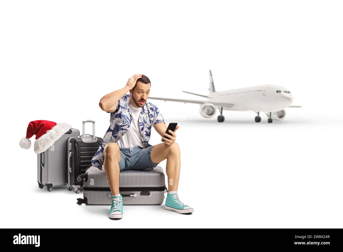 Überraschter männlicher Tourist, der auf einem Koffer sitzt und ein Smartphone vor einem Flugzeug anschaut, weihnachtszeit, isoliert auf weißem Hintergrund Stockfoto