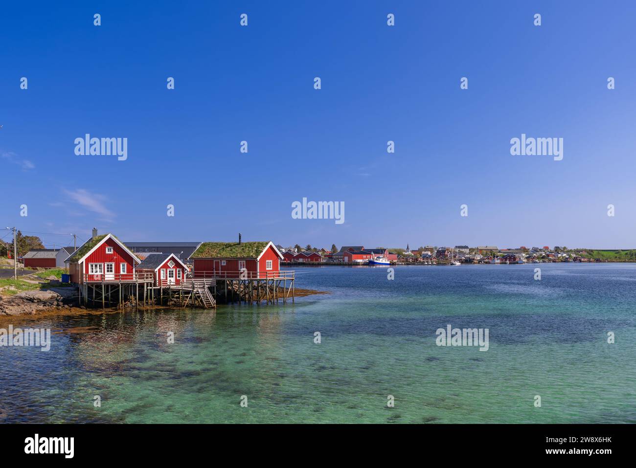 Traditionelle rote norwegische Rorbuer-Hütten stehen auf Stelzen über dem klaren smaragdgrünen Wasser von reine, Lofoten-Inseln Stockfoto