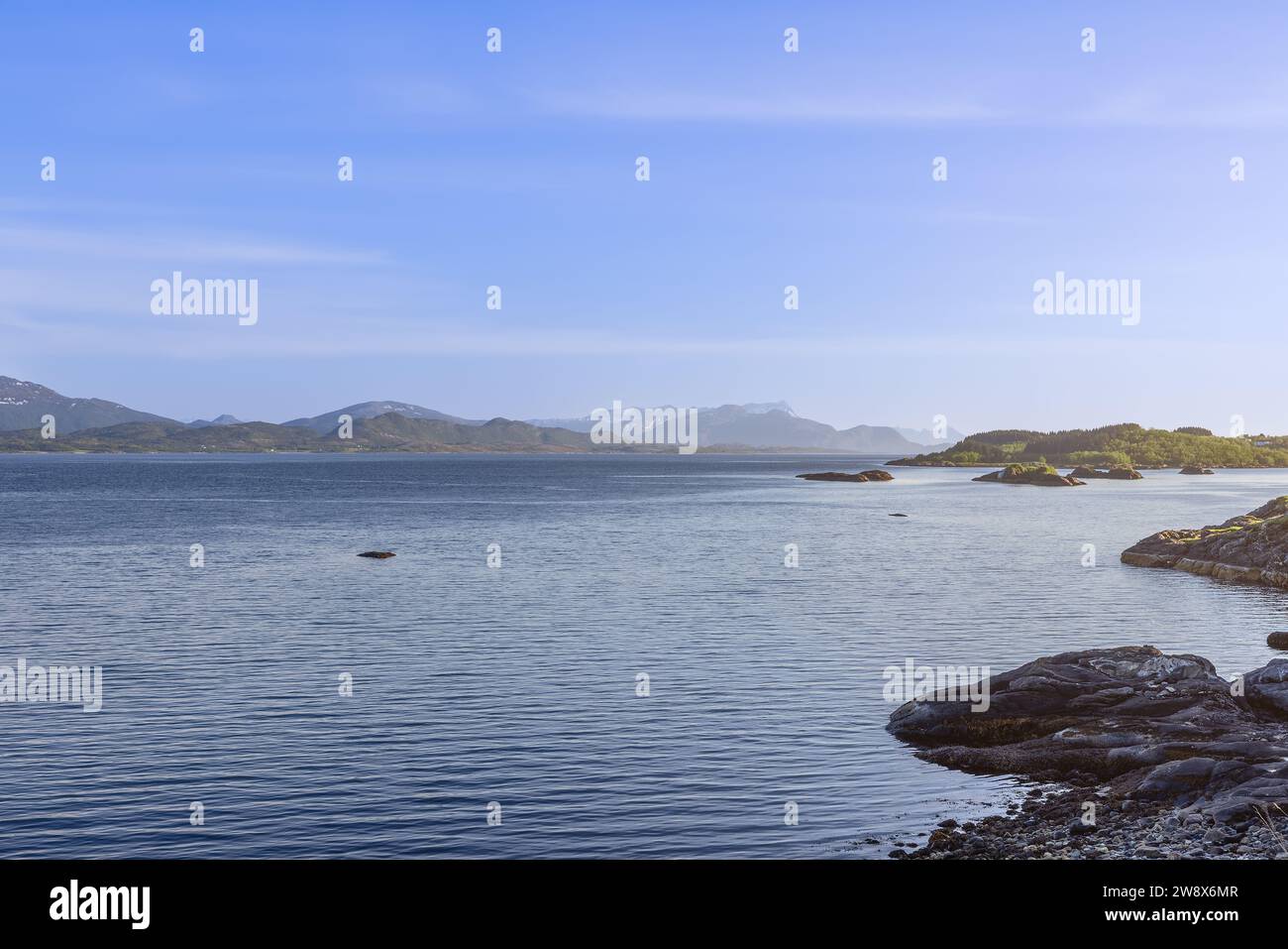 Ruhiges Wasser des Saltfjorden Fjord in der Nähe von Bodo, Lofoten Inseln, Norwegen, das sich in der Sommersonne unter einem klaren blauen Himmel, umgeben von zerklüfteten mountai, sonnt Stockfoto