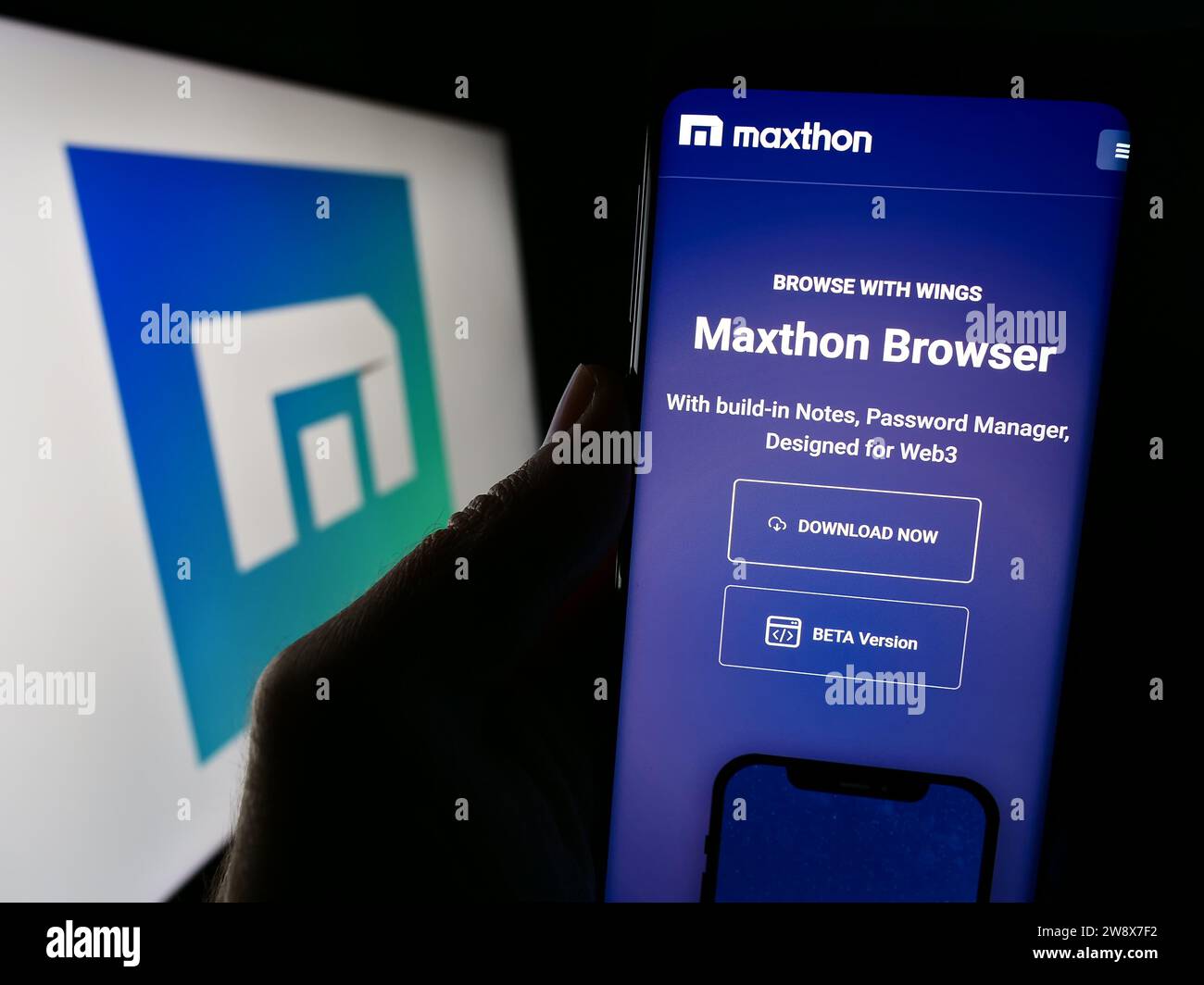 Person, die ein Mobiltelefon mit der Webseite des Webbrowserunternehmens Maxthon vor dem Geschäftslogo hält. Konzentrieren Sie sich auf die Mitte des Telefondisplays. Stockfoto