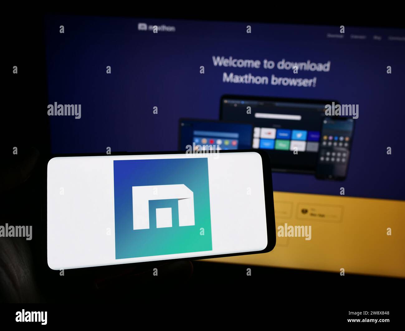 Person, die ein Mobiltelefon mit dem Logo des Webbrowserunternehmens Maxthon vor der Unternehmenswebsite hält. Schwerpunkt auf dem Display des Telefons. Stockfoto
