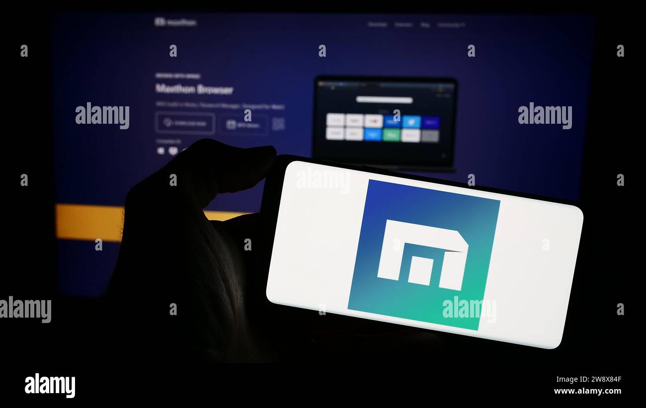 Person, die ein Mobiltelefon mit dem Logo des Webbrowserunternehmens Maxthon vor der Unternehmenswebseite hält. Schwerpunkt auf dem Display des Telefons. Stockfoto