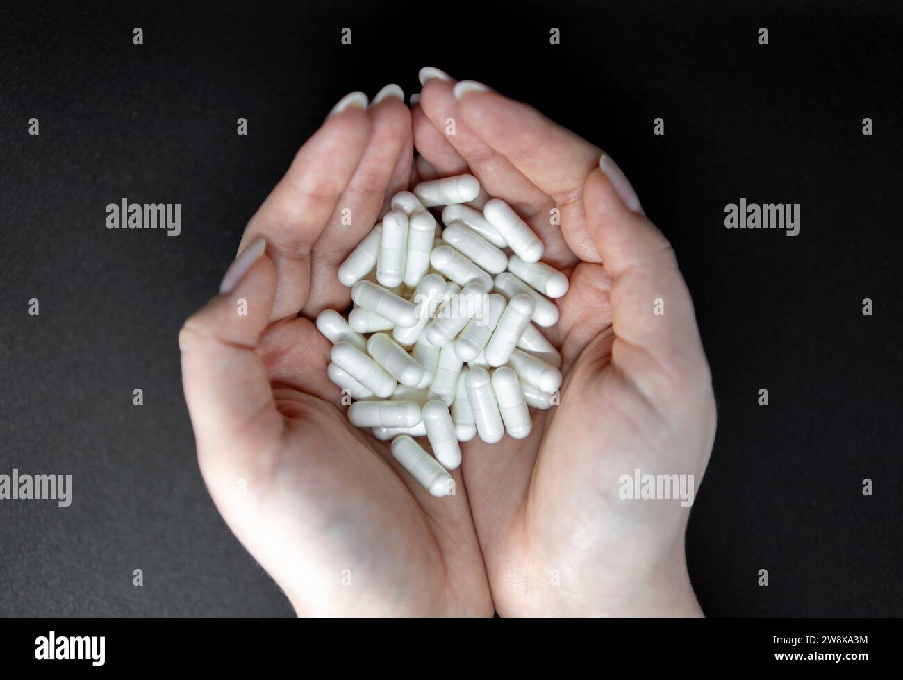 Frauenhände, die Pillen auf schwarzem Hintergrund halten Stockfoto