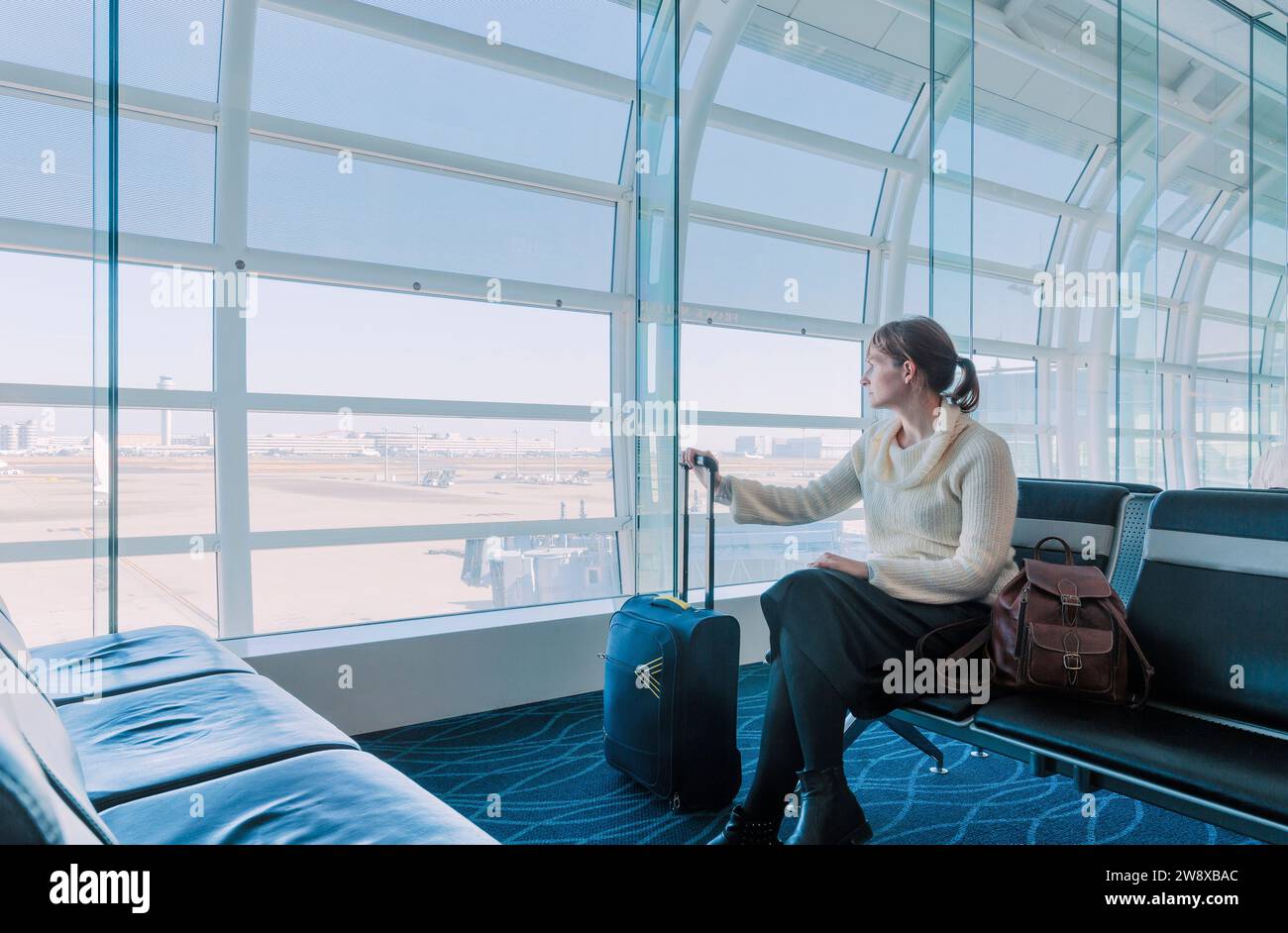 Frau, die aus dem Glas eines Flughafenterminals blickt Stockfoto